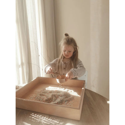 Junges Kind beim sensorischen Spielen mit Getreide in einem Holztablett mit Spielschäufelchen