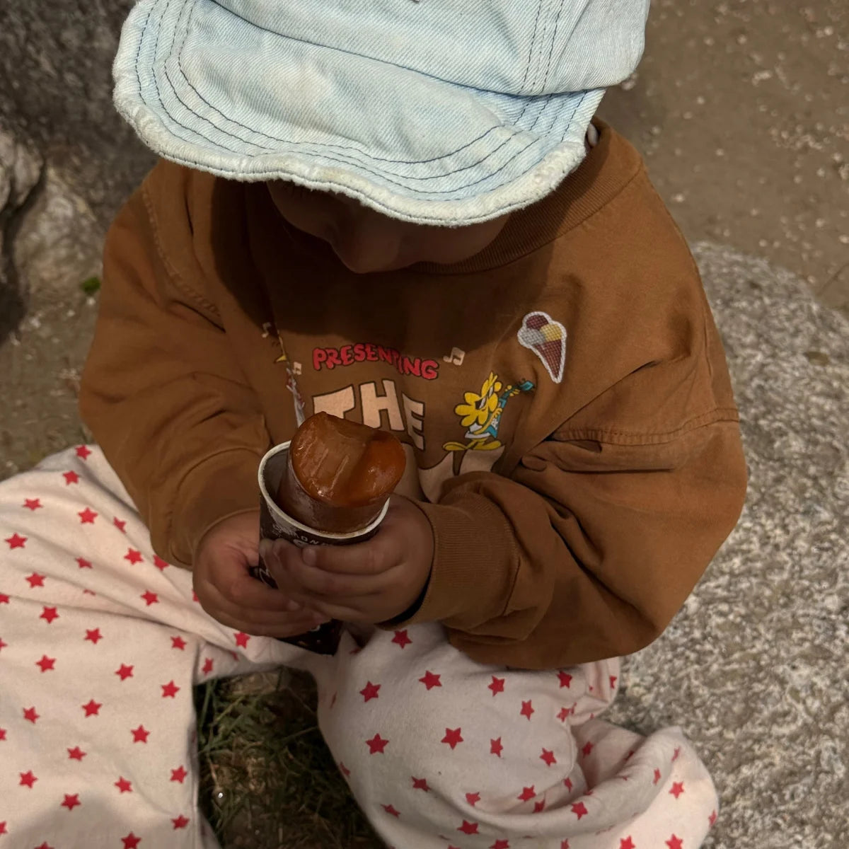 Kleinkind mit Eistüten-Sticker am Pullover sitzt im Garten