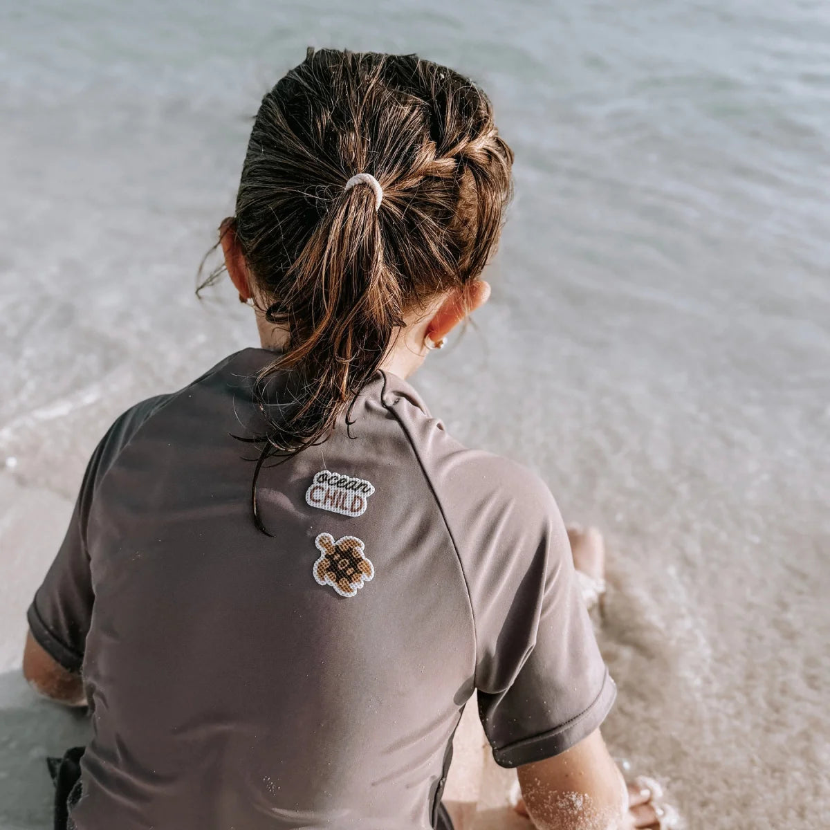 Dunkelgraues kurzärmeliges rashguard aus mückenschutz ocean child edition mit logo und schildkrötenpatch auf der rückseite