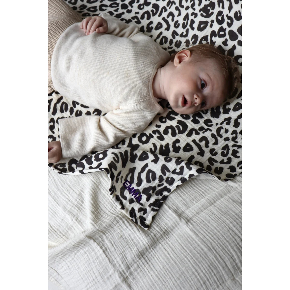 Baby in cremefarbenem Noos Puffy Cross Onesie auf Leoparddecke Mulltuch 120x120cm Holy Cow
