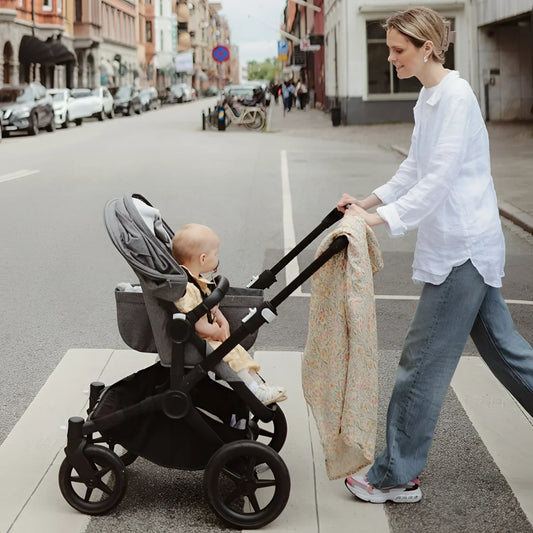 Grauer und schwarzer kinderwagen mit baby und mulltuch in pastel blooms muster