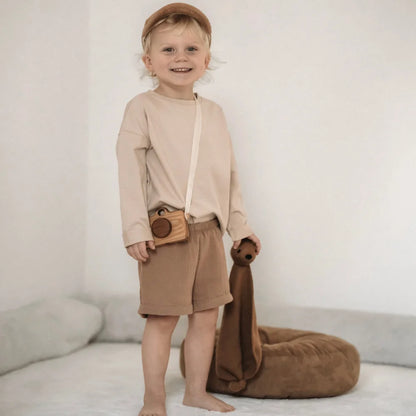 Lächelndes Kind in neutraler Kleidung mit einem Spielzeugbären, Musselin Shorts beige