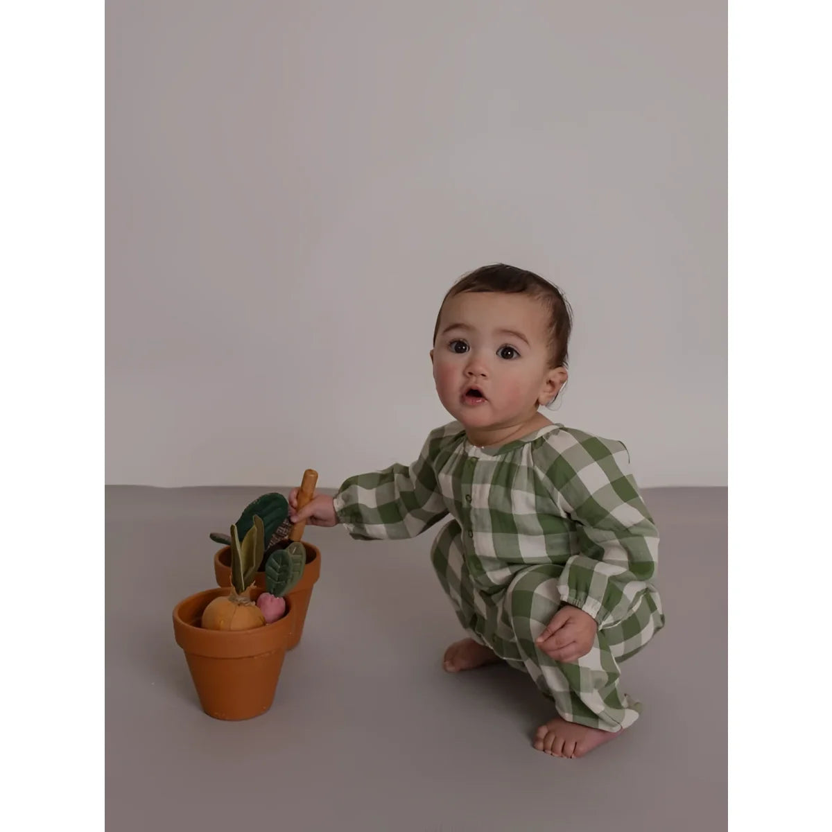 Baby in Onesie Wheat Dill Gingham hockt bei Terrakottatopf mit Spielgemüse