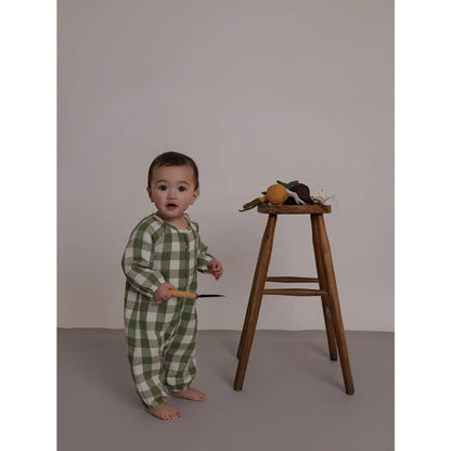 Baby in Onesie Wheat Dill Gingham steht neben Holzhocker