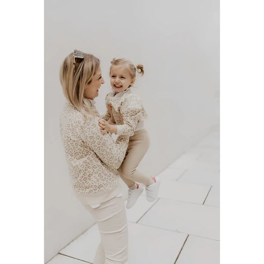 Eine frau trägt einen oversize pullover leo in beige mit leopardmuster und hält ein kind in passender nachhaltiger babykleidung schweiz