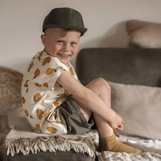Ein kind trägt ein oversized shirt rib zitrone mit orangen zitronenprints und einem dunkelgrünen cap