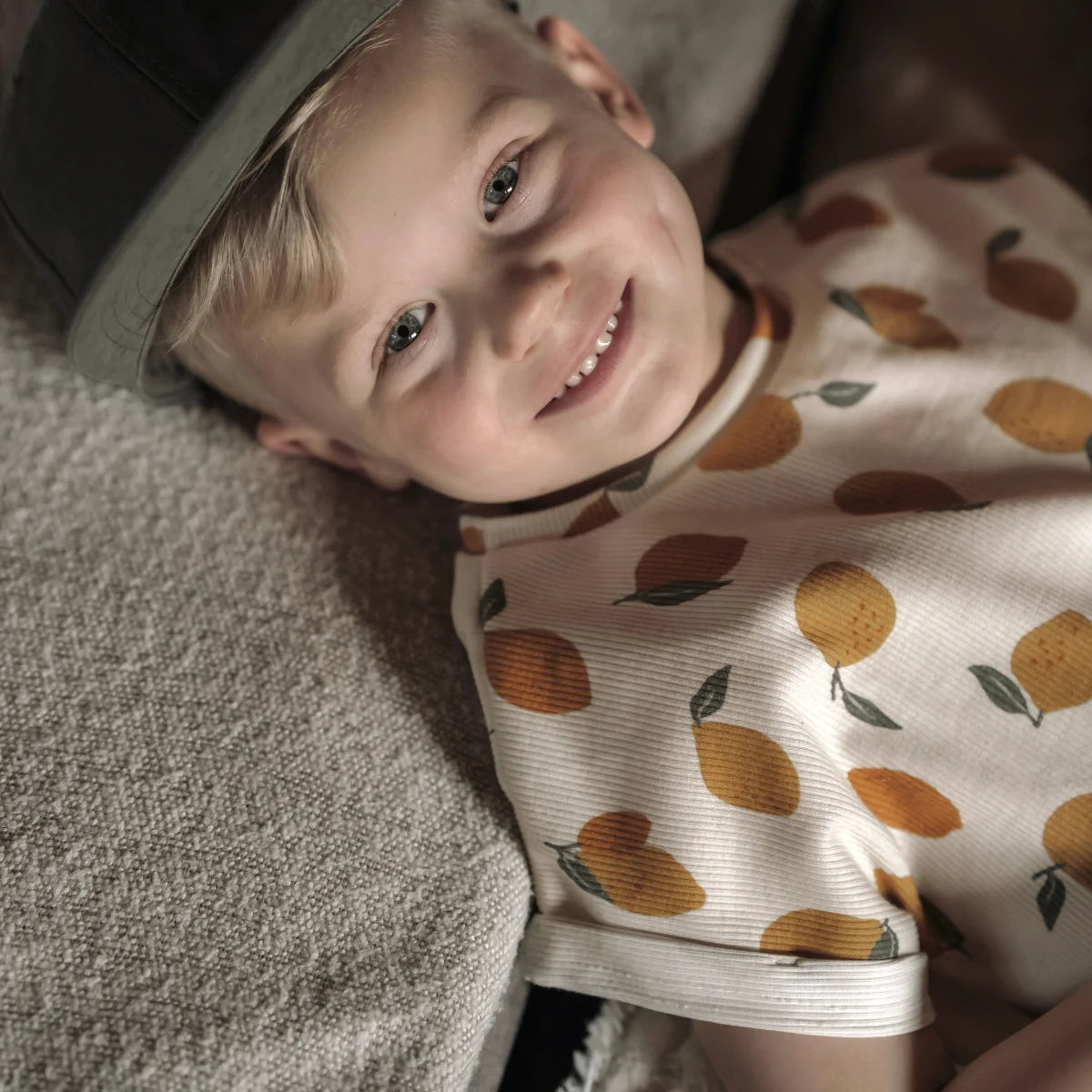Ein kind trägt ein oversized shirt aus ribstoff in creme mit orangefarbenem zitronenprint und kurzen ärmeln