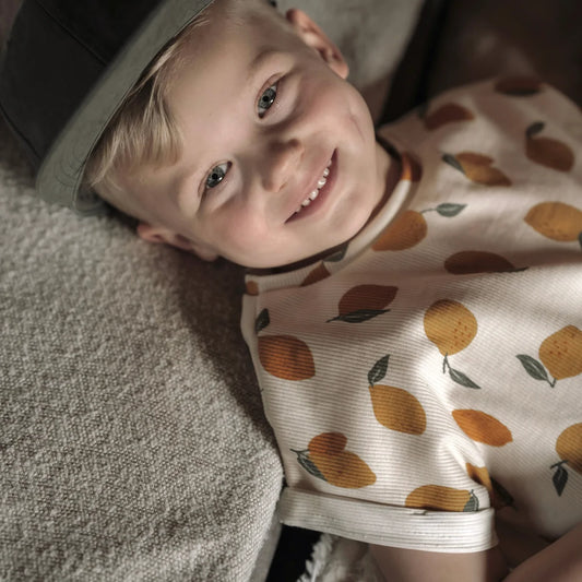 Ein kind trägt ein oversized shirt aus ribstoff in creme mit orangefarbenem zitronenprint und kurzen ärmeln