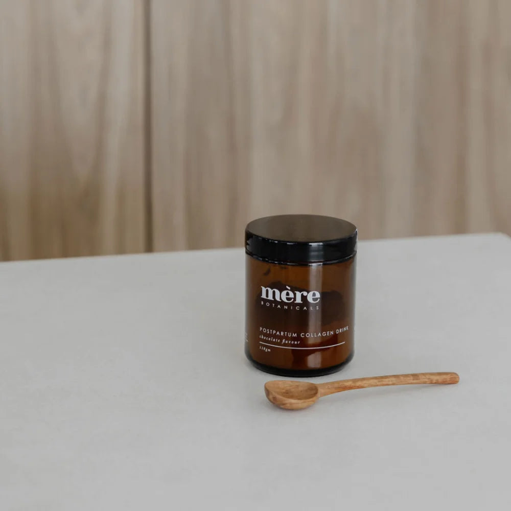 Helles Amberglas mit Collagen-Drink und Holzlöffel, Postpartum Collagen Schokoladengetränk