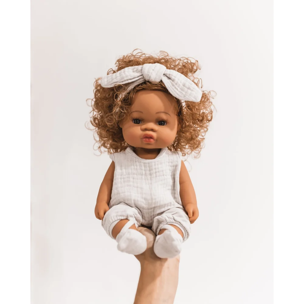 Curly-haired Puppe Loreta doll in a white outfit with bow headband