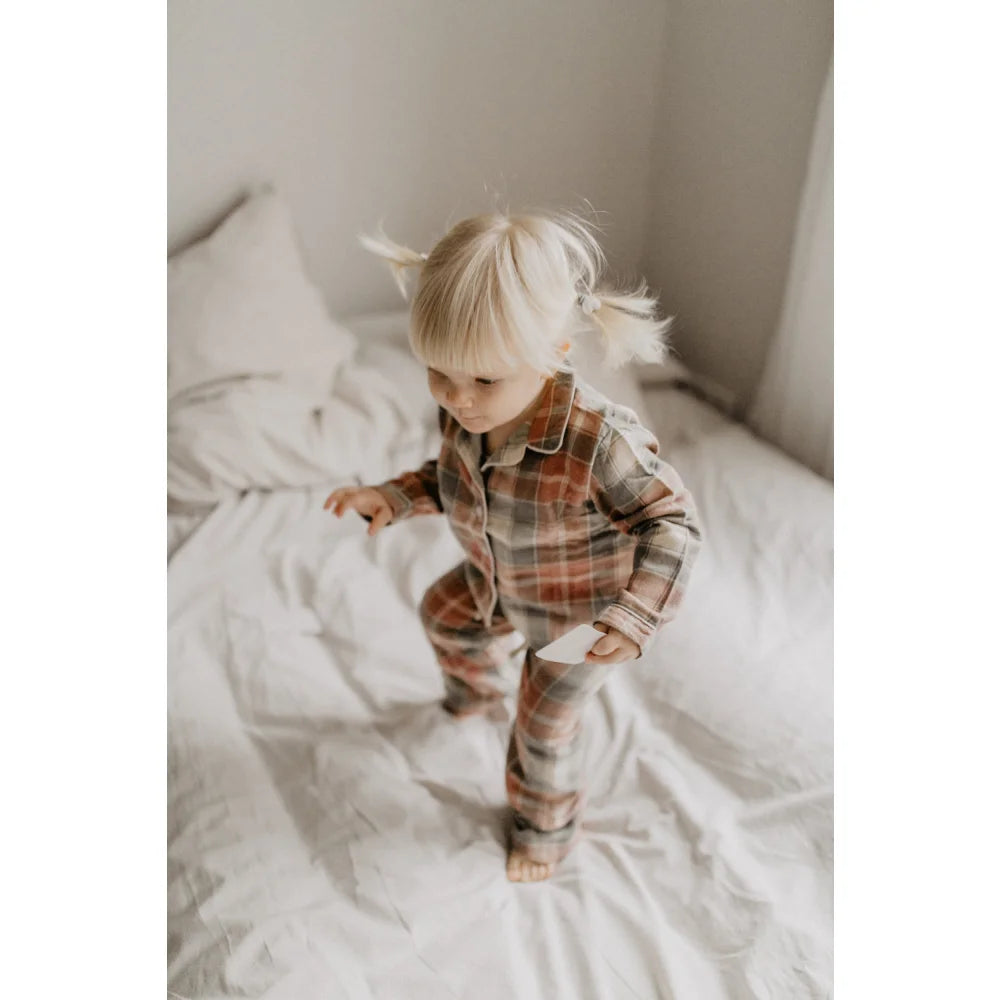 Kleiner Junge trägt rote grüne Flanellpyjama mit Zöpfen und weißen Haarband