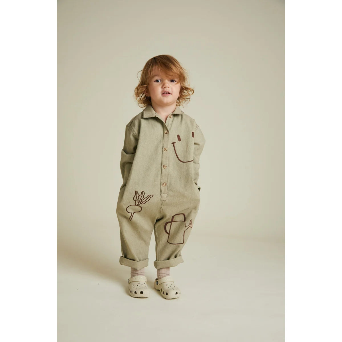 Ein beige overall quinn olive allotment mit langen ärmeln und stickereien von lachgesichtern und gartengeräten