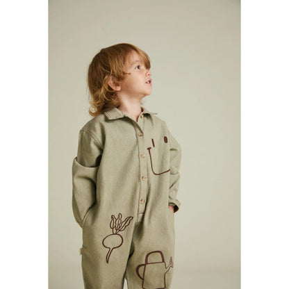 Ein kind trägt ein sagegrünes, langärmeliges overall mit braunen linienzeichnungen von gemüse und gartenwerkzeug