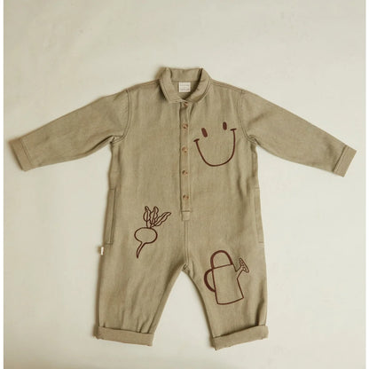 Beige langärmiger baby-strampler quinn olive allotment mit braunen stickereien von lächelndem gesicht, rote bete und gießkanne