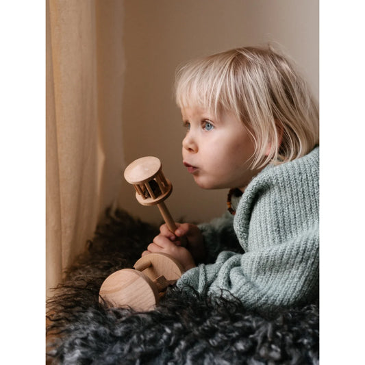 Ein kind hält eine hellfarbene holz-rassel rassel nighthawk aus nachhaltigen baby- & kinderprodukten