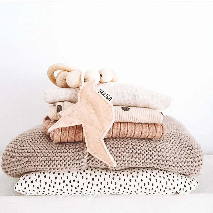 Gestapelte neutralfarbene Babykleidung für das Produkt Rassel Vogel Blush