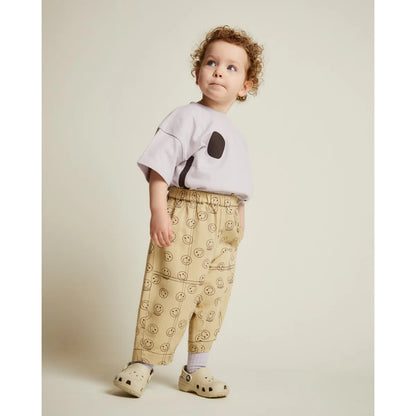 Kind trägt beige rex joy butter hose mit elastischem bund und hellgrauem t-shirt mit schwarzem patchdesign