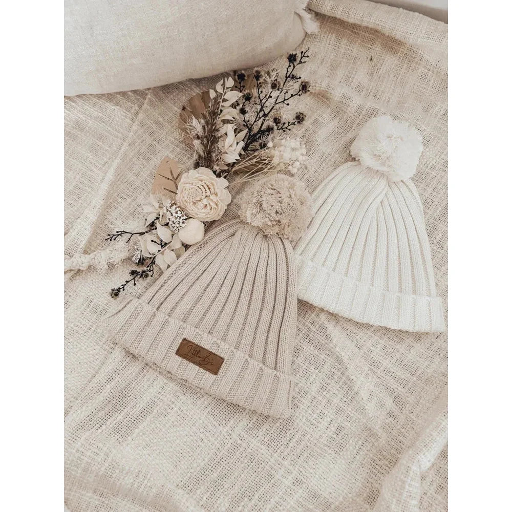 Ribbed Beanie in Milk color displayed with knitted pom-pom hats and getrockneten Blumen