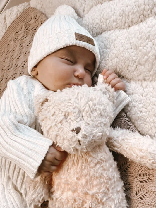 Schlafendes Baby umarmt einen plüschigen Teddybär im Ribbed Beanie Milk