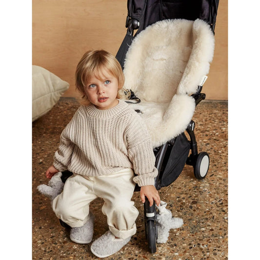 Junges Kind in Strickpullover und kuscheligen Hausschuhen vor dem Schaffell Snuggler Milk