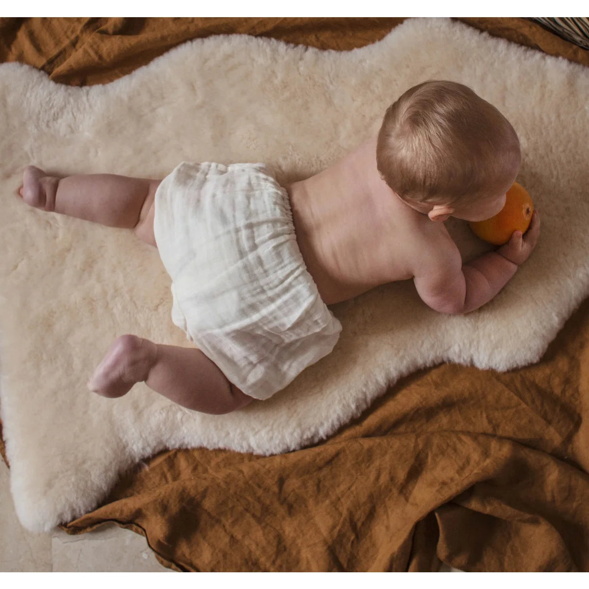Baby auf einem Teppich mit einer Orange, Schaffell Snuggler Leopard Peanut