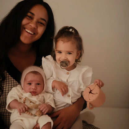 Lächelnde Frau mit zwei kleinen Kindern, einer mit Schnuller aus Silikon