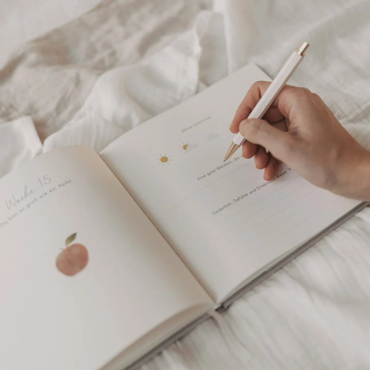 Schwangerschaftstagebuch mit eleganter weißer Feder in Hand gehalten