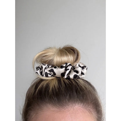 Kuhprint Scrunchie Fable mit schwarz-weißen Flecken auf hellem braunem Haarknoten