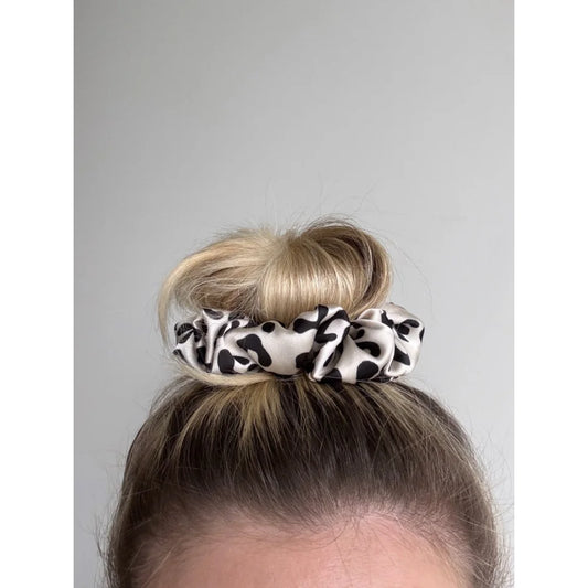 Kuhprint Scrunchie Fable mit schwarz-weißen Flecken auf hellem braunem Haarknoten