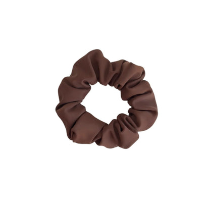 Ein weiches, mattes braunes stoffscrunchie mit geraffter, gerippter textur aus der mini + me | mocha kollektion