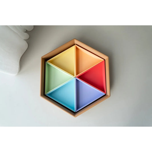 Sechseckige mandigo spielschale aus holz mit sechs pastellfarbenen dreieck-einsätzen in gelb, orange, grün, rot, blau und lila