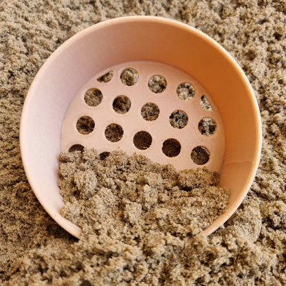 Peachfarbener Kunststoffsieb mit perforiertem Boden, teilweise gefüllt mit feinem Sand