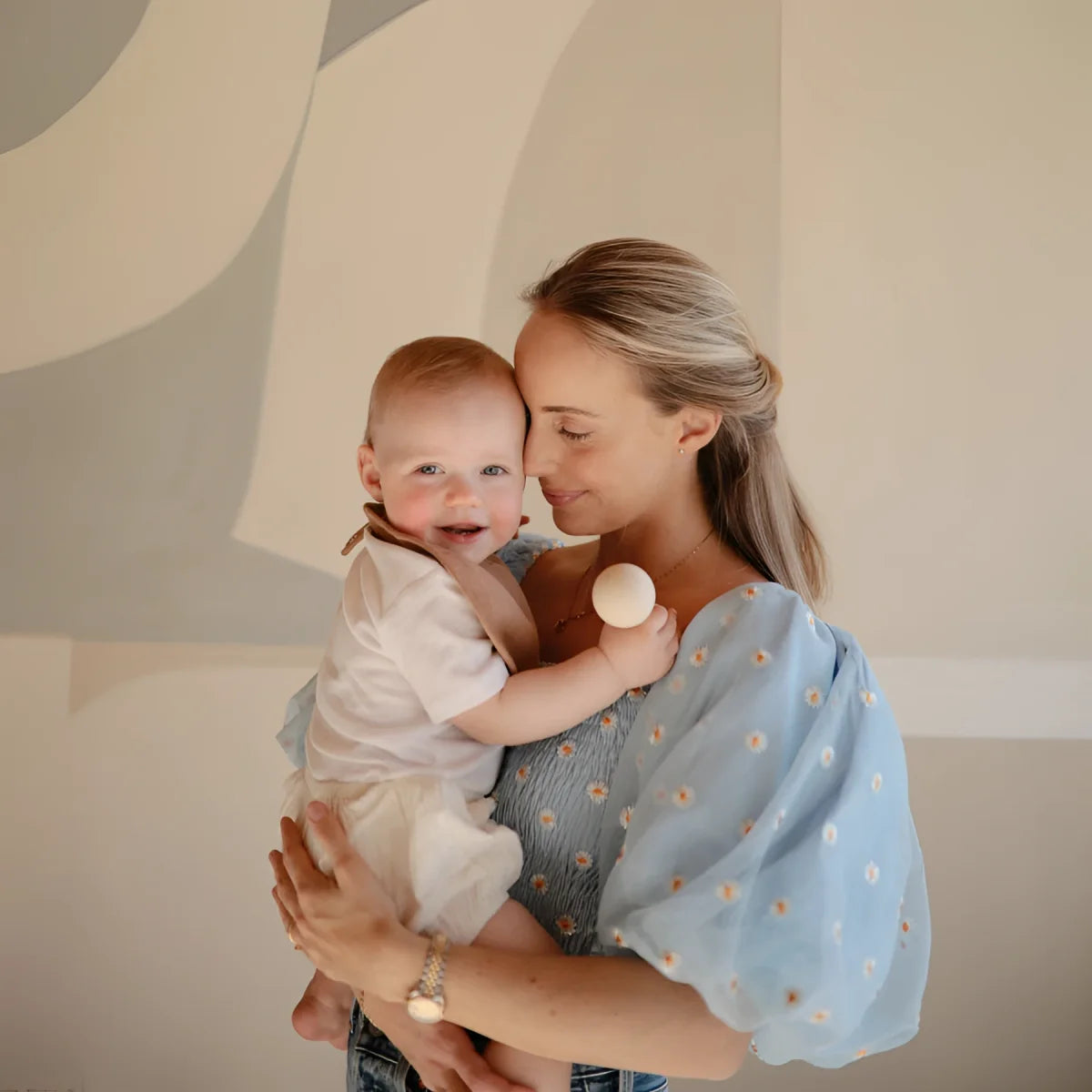 Mutter umarmt lächelndes Baby mit Silikon Baby Rassel in Sand oder Naturfarbe