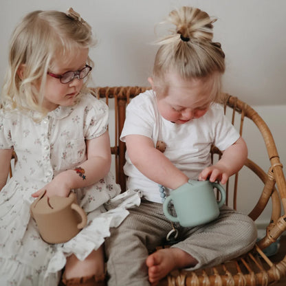 Zwei junge Kinder in einem Korbsessel mit Snack Becher in Naturfarben