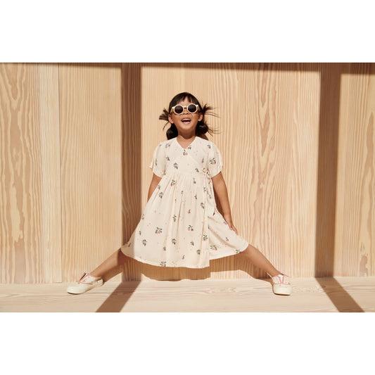 Kind in cremefarbenem Kleid mit Blumenmuster und Darla Sonnenbrille aus recyceltem Polycarbonat mit polarisierten Gläsern