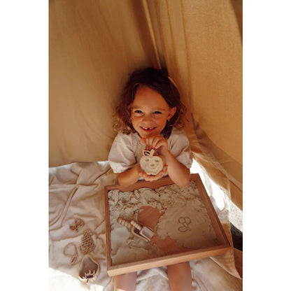 Lächelndes junges Mädchen hält das spielzeugähnliche Spielschäufelchen mit Apfelform und Blatt