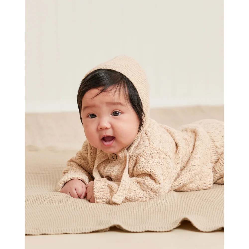 Baby auf Decke in beigem Outfit, passend zur Strickmütze Shell