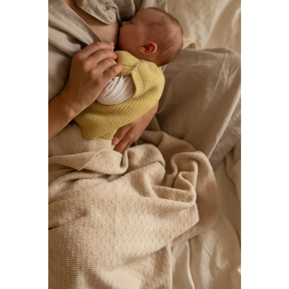 Neugeborenes Baby im gelben Pullover auf weichem Bettzeug in jemandes Armen