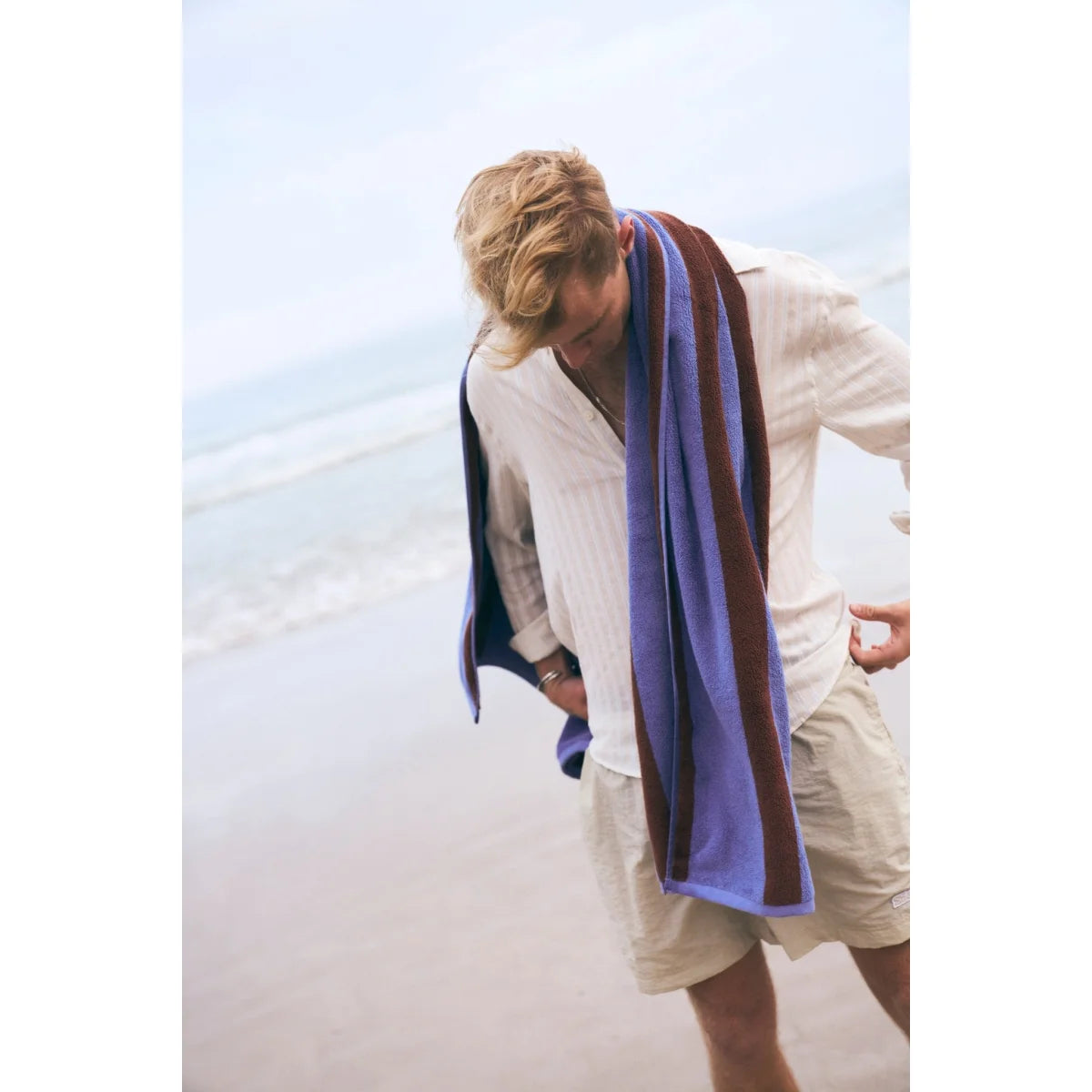 Ein blau und bordeaux gestreiftes stripes badetuch aus nachhaltiger materialien getragen auf den schultern eines mannes ideal für ökologische baby- & kinderprodukte und geschenke für neugeborene