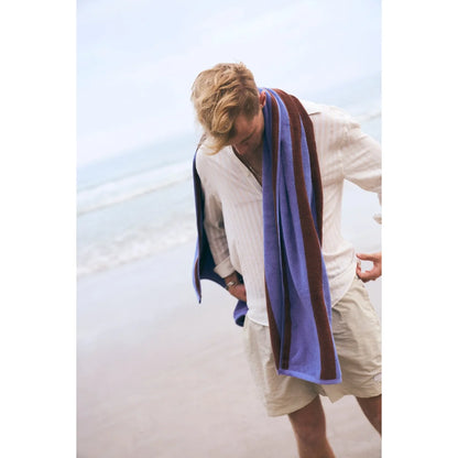 Ein blau und bordeaux gestreiftes stripes badetuch aus nachhaltiger materialien getragen auf den schultern eines mannes ideal für ökologische baby- & kinderprodukte und geschenke für neugeborene