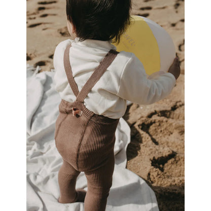 Baby in braunen Strumpfhosen mit Trägern am Strand von Granola