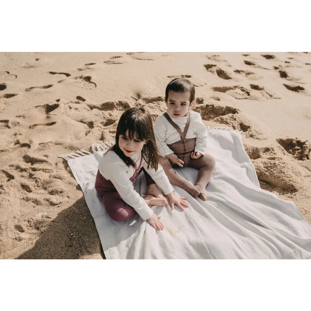 Zwei Kinder auf einer weißen Decke am Sandstrand mit Strumpfhose mit Träger