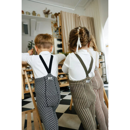 Zwei Kinder in passenden weißen Hemden mit Trägern über karierten Strumpfhosen