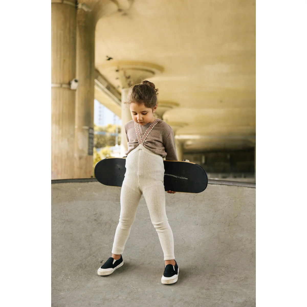 Junges Mädchen mit Skateboard trägt Strumpfhose mit Träger in Cremefarben