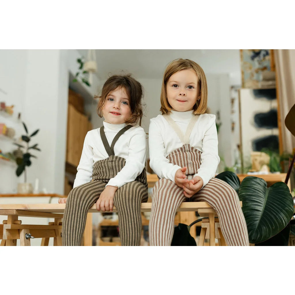 Zwei junge Mädchen in passenden weißen Rollkragen-Shirts und Granola-Creme-Streifen-Trägerhosen