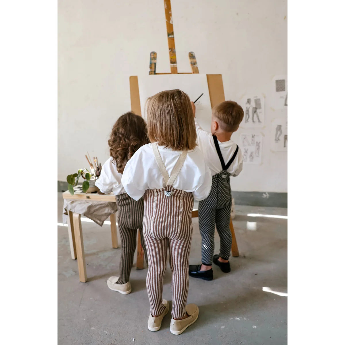 Kinder in gestreiften Strumpfhosen mit Trägern Granola x Cream, weiße Hemden, Hosenträger, beige Schuhe