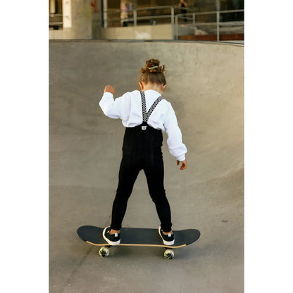 Junger Skateboarder in weißem Shirt und schwarzen Overalls auf einem Skateboard