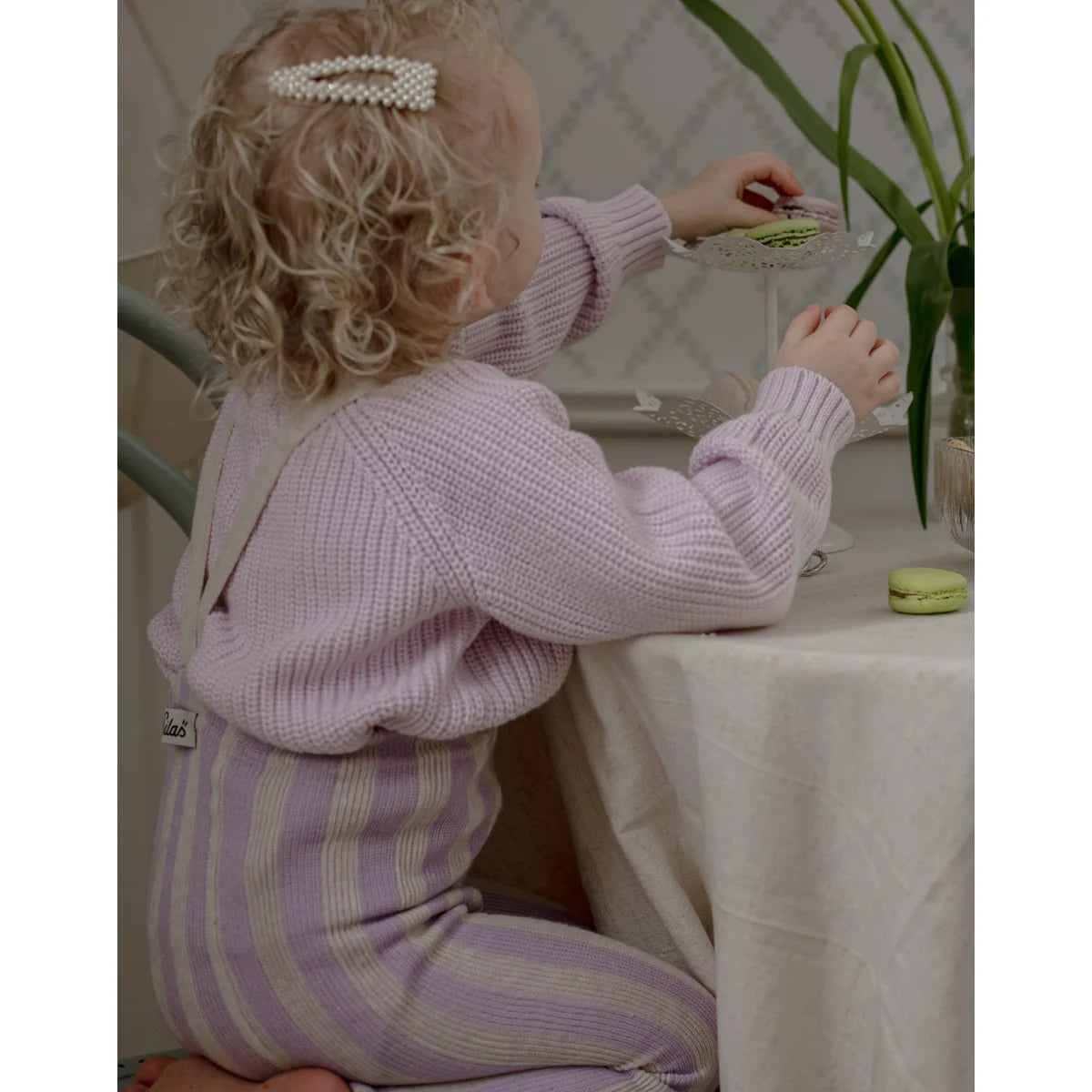Ein kind trägt eine strumpfhose mit träger footless in lavendel und creme aus gestricktem material mit perlenhaarclip