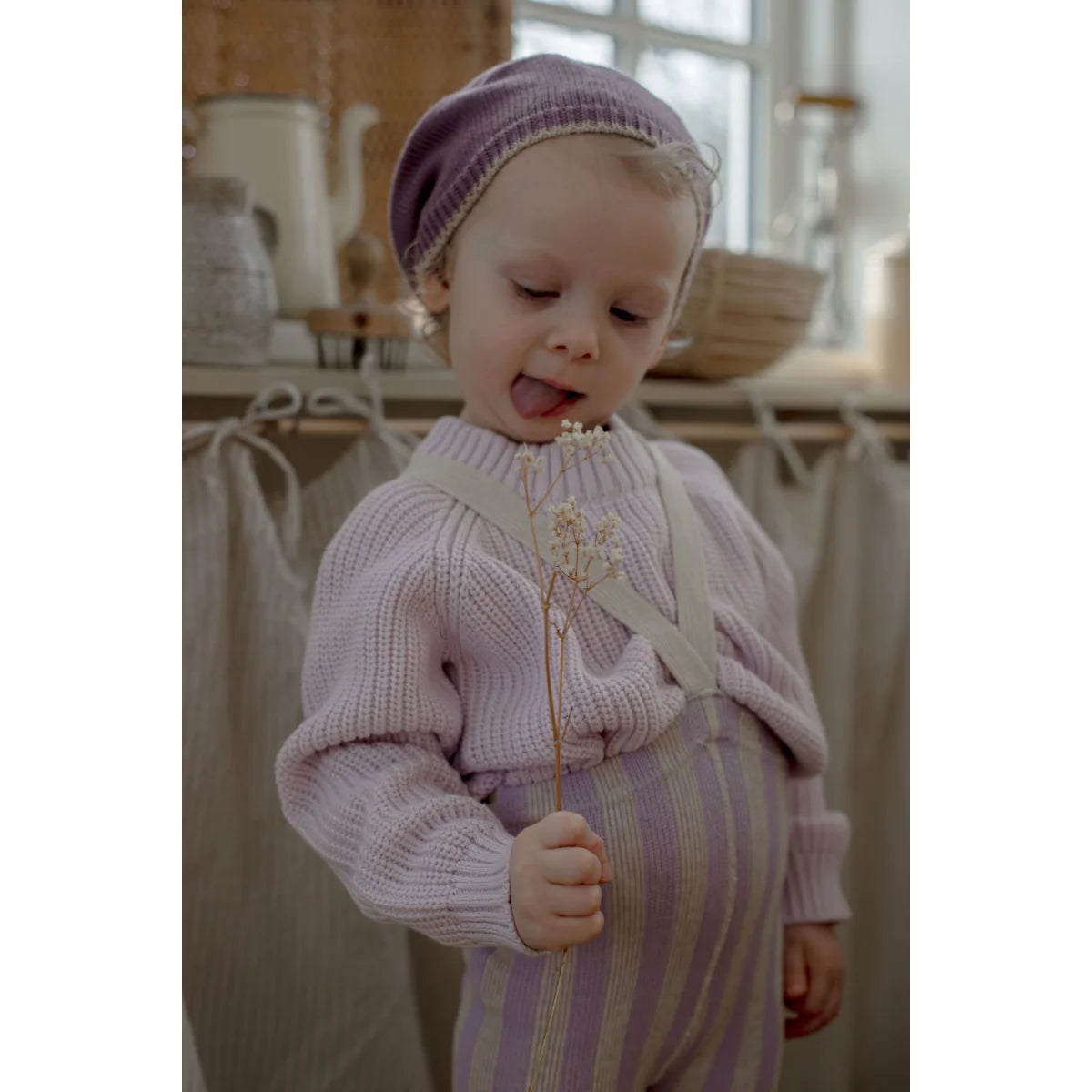 A young child wears lavender x cream footless strumpfhose mit träger in soft knit holding dried flowers