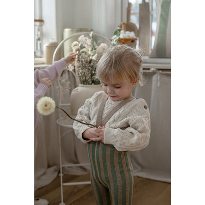 Kind strumpfhose mit trägern footless in matcha und peanut mit cremefarbenem zopfstrickpullover und gestreifter latzhose